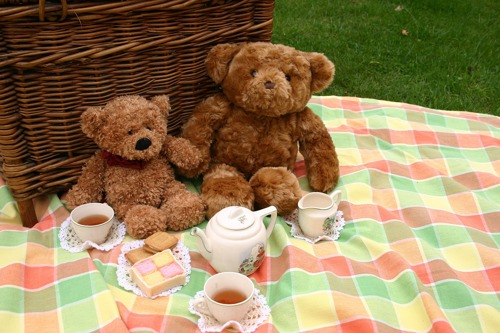 Two teddy bears enjoying a picnic together including tea and cake
